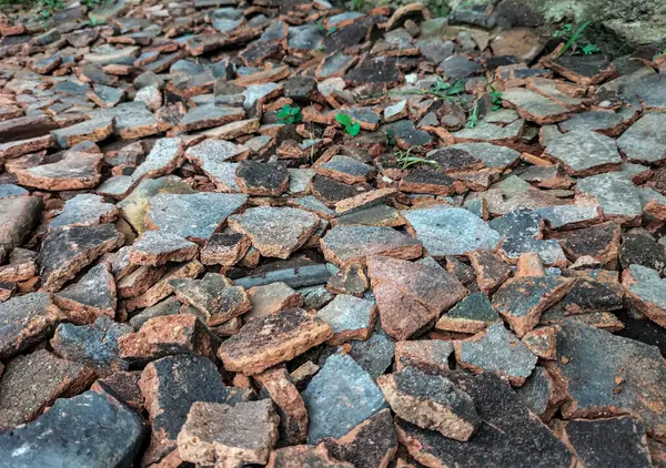 Seçici odaklanma. Kırık çatı döküntüleri, taşlar ve küçük çakıllarla birlikte yere saçılmış ve doğal pürüzlü bir dokuyla bir yüzey oluşturmuştur. Kullanılmayan kırmızı çatı kiremitleri.
