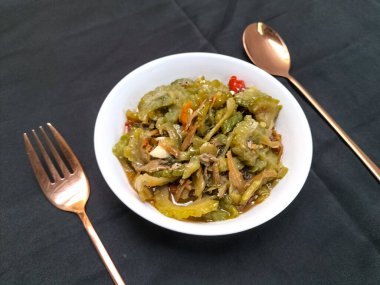 Beyaz kasede ançüezli kızarmış kavun görüntüsü. İçindekiler arasında acı kavun, ançüez, biber, şeker, tuz ve balık sosu yer alıyor. Endonezya yemekleri.