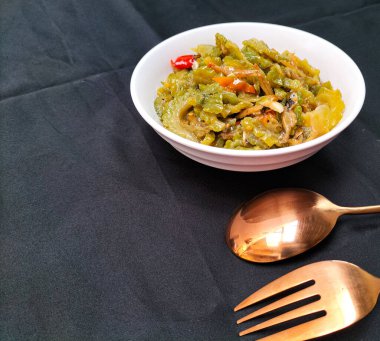 Beyaz kasede ançüezli kızarmış kavun görüntüsü. İçindekiler arasında acı kavun, ançüez, biber, şeker, tuz ve balık sosu yer alıyor. Endonezya yemekleri.