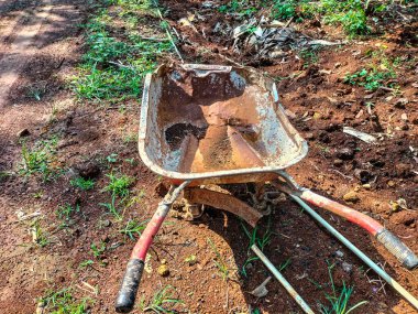 Bahçedeki toprak yığını üzerinde eski, kirli ve paslı tek teker arabası. Metal tramvay. Seçici odak.