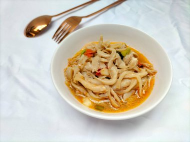 Seçici odaklanma. Karıştırılmış istiridye mantarı ya da midye reçeli tiram. Tadı daha taze olsun diye domatesle servis ediliyor ve beyaz arka planlı beyaz bir kasede servis ediliyor. Kaşık ve çatal..