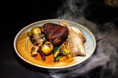 Tütsülenmiş Polonya usulü biftek, yanında da Masurian levreği ve sebze.