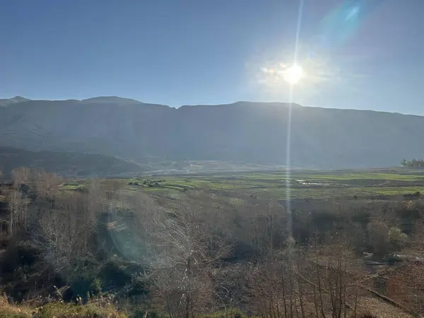 Dağların üzerinde parlayan güneşli bir vadi manzarası