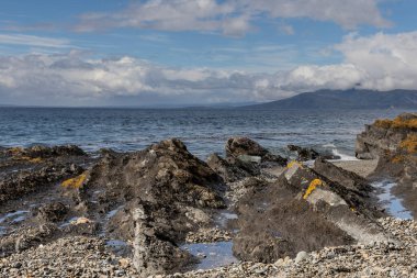 Dağlar ve bulutlu gökyüzü ile kıyıda kaya oluşumu