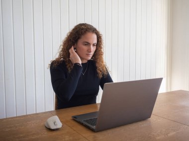 Kızıl saçlı kadın bilgisayarla çalışırken saçına dokunuyor.