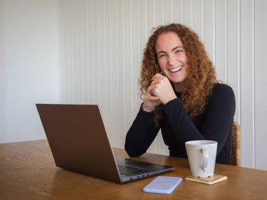 Bir fincan çay içerken evde çalışmaktan mutlu olan kızıl saçlı genç bir kadın.