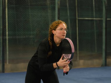 Kararlı bir kadın açık hava tenis kortunda elinde pembe raketle hazır bekliyor.