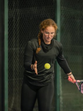 Aktif kıyafetli bir kadın, konsantrasyon ve beceri sergileyen bir Padel tenis maçına hazırlanıyor.