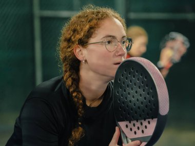 Yoğun bir açık hava oyununda servis yapmaya hazırlanan, elinde raketle odaklanmış dişi bir Padel oyuncusunun yakın çekimi.