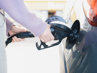 Yakından birinin elleri yakıt pompası hortumunu tutarken, gün ışığında benzin istasyonunda gümüş bir arabaya yakıt doldururken.