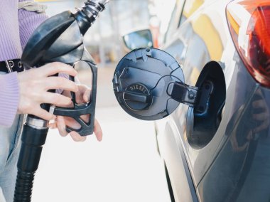 Yakından çekilen ellerde dizel yakıt pompası var. Gümüş bir arabanın yakıt deposuna yerleştiriliyor. Enerji ve ulaşımı vurguluyor.