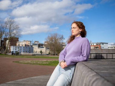 Mor kazaklı, rahat bir genç kadın, güneşli havanın tadını çıkarıyor. Gözleri kapalı, sakin bir şehir parkında oturuyor.
