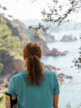 Costa Brava 'nın dingin ve kayalık kıyılarına bakan bir kadının arka görüntüsü, Katalonya' nın doğal güzelliğine dalmış.