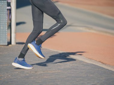 Dinamik görüntü bir koşucunun bacaklarını ve mavi spor ayakkabılarını açık pistte yakalıyor.