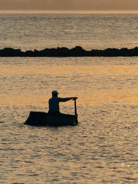 Da Nang 'da Sunset' te küçük bir teknede tek başına yüzen Asyalı adam.