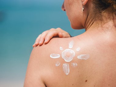 Güneş kremi sürerek, plaj güneşinin altında cilt korumasını vurgulayan bir kadının sırtına yakın çekim.