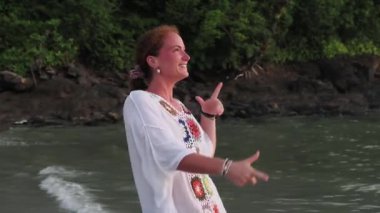 Beyaz elbiseli genç bir kadının el kamerasıyla Langkawi, Malezya 'nın güzel plajında dans edişinin ve gülümsemesinin videosu. Mutluluğun ve anın tadını çıkarıyor. Seyahat ve eğlence konsepti