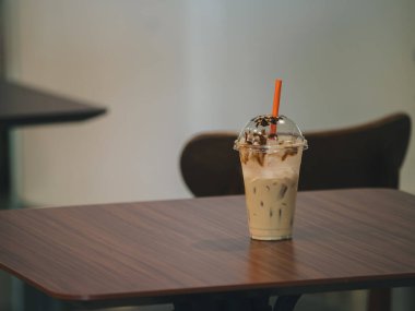 Karamelli ve kırmızı pipetli lezzetli bir köpüklü süt çayı, plastik bir fincanda servis edilir, rahat bir kafe ortamında ahşap bir masanın üzerine konur.