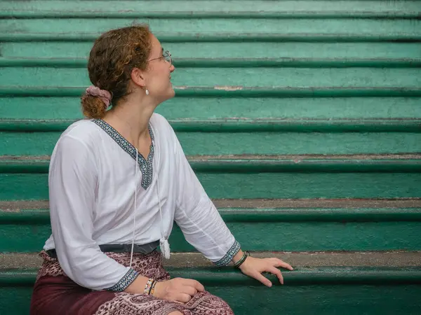 stock image A thoughtful tourist sits on the green steps at Batu Caves, Malaysia, looking to the side and enjoying a reflective moment during her cultural exploration