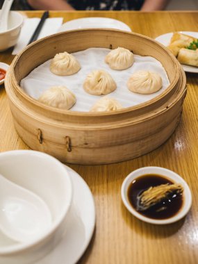Tahta bir masada taze buğulanmış hamur köfteleriyle dolu bambu budan bir sepet, yanında da dilimlenmiş zencefil ve beyaz sofra takımı ile küçük bir tabak soya sosu. Otantik Çin mutfağı