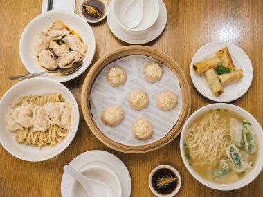 Bambu sepetinde buharda pişirilmiş hamur köfteleri, hamur köfteleri, börekler ve ahşap bir masaya konmuş bir kase köfte çorbası gibi çeşitli Çin yemeklerinin genel görünümü. Geleneksel Asya ziyafeti