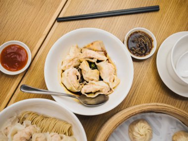 Çeşitli Çin yemeklerinin genel görünümü. Baharatlı sos, erişte ve küçük soslu hamur köfteleri de dahil. Ahşap bir masada yemek çubuklarıyla. Çeşitli Asya yemekleri