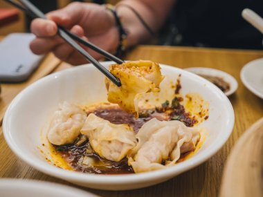 Bir el yemek çubuğu, baharatlı soslu hamur köftesiyle dolu bir kaseden ahşap bir masaya yerleştirilmiş bir hamur köftesi alır. Lezzetli Asya mutfağı