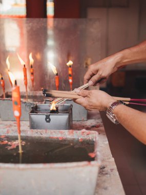 Tapınaktaki mumlardan tütsü yakan ellerin yakın çekim görüntüsü, adanmışlık ve hürmetle ruhani bir tören gerçekleştirmenin samimi eylemini yakalıyor.