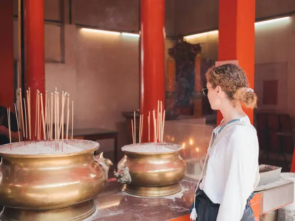 stock image A woman with curly hair and sunglasses contemplates a large incense burner in a Buddhist temple, embracing a reflective moment of spiritual connection and tranquility