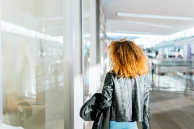 Afro saçlı genç siyah kız bir alışveriş merkezinin vitrininde yürüyor. Arkasını döndü ve yüzü tanınmaz halde..