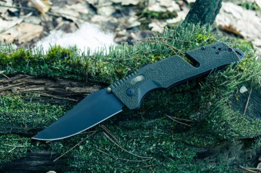 Keskin bir askeri bıçak ve siyah bir bıçak. Ormandaki yosunlara yeşil saplı bir bıçak. Ön görünüm.