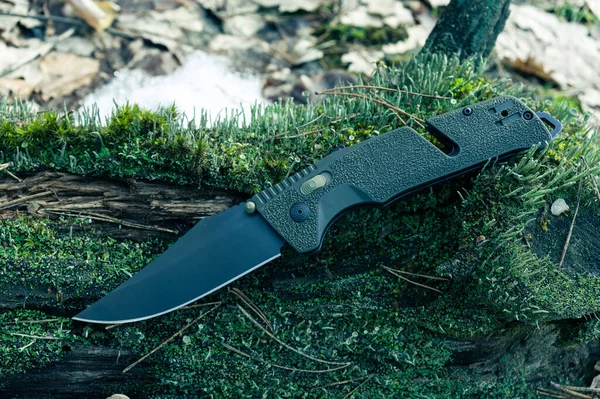 黒い刃の鋭い軍用ナイフ 森の苔に緑の柄のナイフ 正面図 — ストック写真