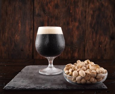 Bir bardak koyu bira alayım. Koyu bira ve fıstık. Bira ve atıştırmalık servisi. Ahşap arka plan. Ön görünüm.