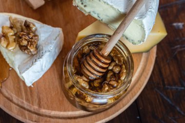 Ballı ve cevizli cam kavanoz. Bal kavanozunda bal kaşığı. Bal ve peynir. Makro fotoğraf üst görünümü. Ahşap arkaplan.
