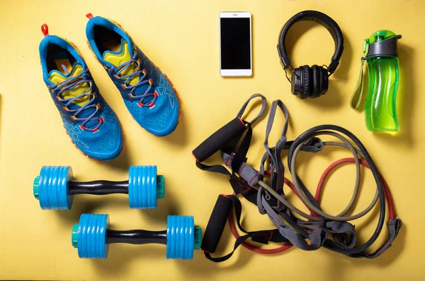 Running shoes and a variety of cardio and fitness items. Fitness at home on the mat. Objects on a yellow background. View from above.