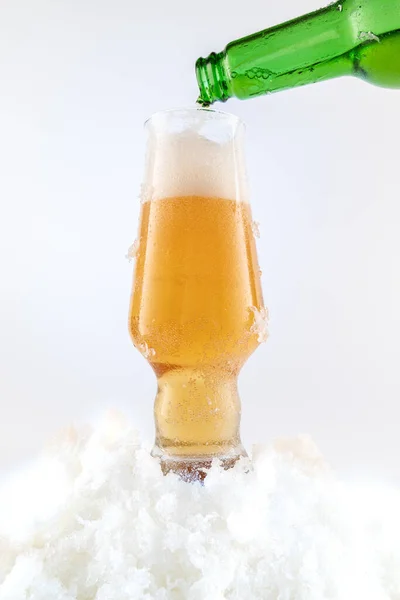 Pouring draft beer into a glass. A glass of beer and snow. Cool beer. Vertical frame.