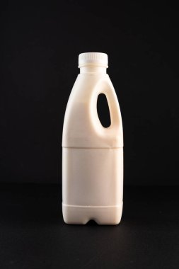 Bottle of milk with a handle. White bottle on a black background. Vertical frame.
