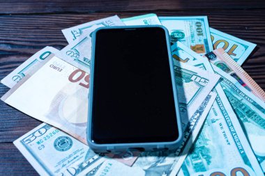 Akıllı telefon ve çeşitli para birimleri masada. Telefon aracılığıyla döviz değişimi. Akıllı telefondaki finans. Açı ön görünümü.