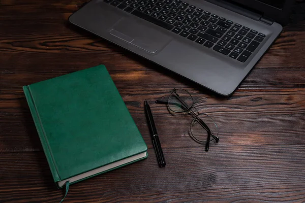 stock image Green diary on the table. Diary and laptop. Notepad, laptop and glasses. Keep a diary entry. Top view at an angle.