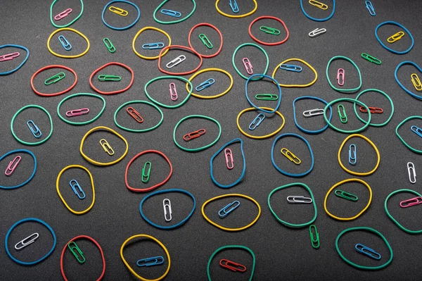 Background from stationery items. The background is slanted. Falling rubber bands and paper clips. On a black background.