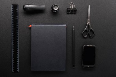 Masadaki ofis malzemelerini güzelce düzenledim. Siyah bir masada siyah nesneler. Masaüstünde sipariş verin. Yukarıdan görüntüle.