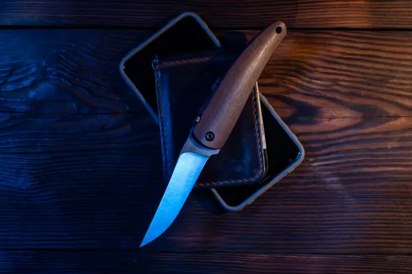 Folding pocket knife and wallet on the table. A sharp knife with a wooden handle. Knife on the table. Top view.