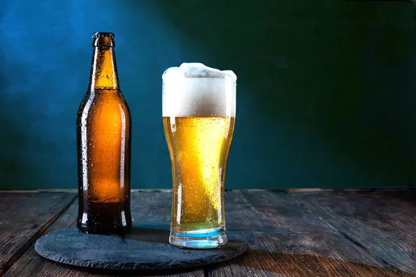 Bir şişe soğuk bira. Bir bardak soğuk bira. Masada bira var. Tepside bira servisi. Ön görünüm.