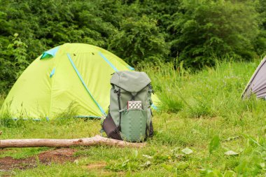 Turist çadırının arka planında duran yeşil turist çantası. Çadırlı ve teçhizatlı bir turist kampı. Ön görünüm.