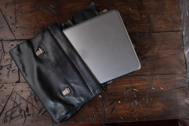 Masada deri iş çantası var. Çanta ve dizüstü bilgisayar masada. Evrak çantası ve laptop ahşap bir masada..