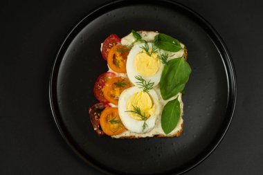 Siyah tabakta diyet sandviç. Haşlanmış yumurtalı, domatesli ve yeşillikli sandviç. Renklerin zıttı. Yukarıdan görüntüle.
