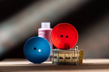 Kırmızı ve mavi dikiş düğmeleri, renkli iplikler ve açık bir yüzeye yerleştirilmiş bant ölçüm bantları içeren yaratıcı yakın plan fotoğraf..