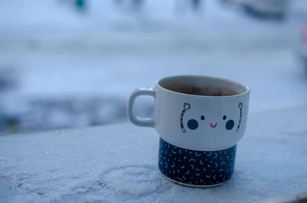 Funny cup of coffee in the snow outside the window