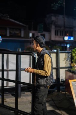 Jakarta, Indonesia - October 2 2023: Man in Vest Using Phone on Street