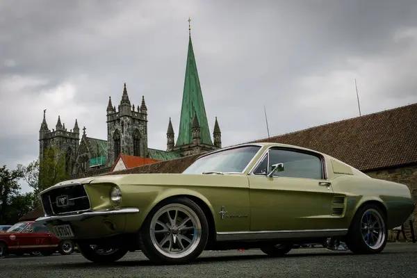 Canlı yeşil bir Mustang, modern tarzla geleneksel mimariyi harmanlayan antika bir kilisenin önüne park edilmiştir.